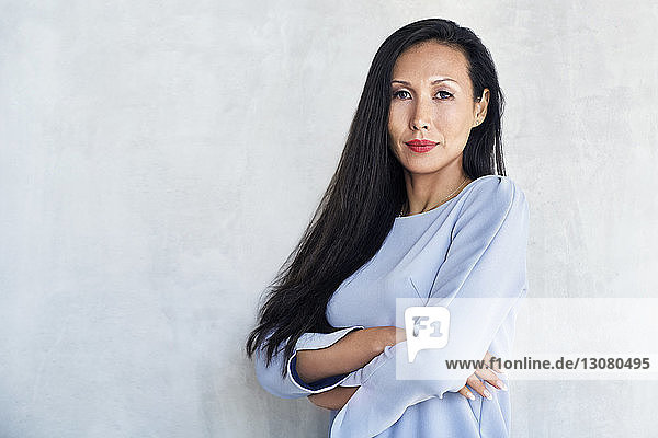 Porträt einer selbstbewussten Geschäftsfrau  die die Arme gegen die Wand verschränkt