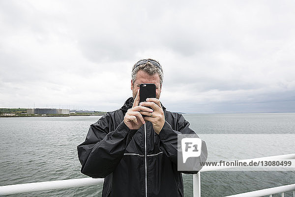Man photographing while standing by railing against sea