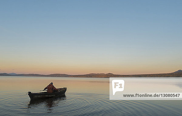 Hochwinkelaufnahme eines Mannes in einem Boot auf dem See vor klarem Himmel bei Sonnenuntergang