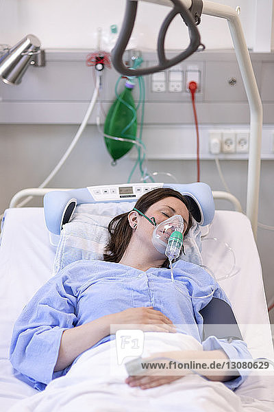 High angle view of female patient wearing oxygen mask while sleeping on bed in hospital