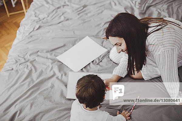 Hochwinkelaufnahme einer glücklichen Mutter und eines kleinen Jungen mit Schulsachen auf dem Bett zu Hause