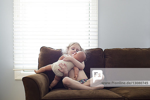 Mädchen spielt mit Puppe  während sie zu Hause auf dem Sofa sitzt