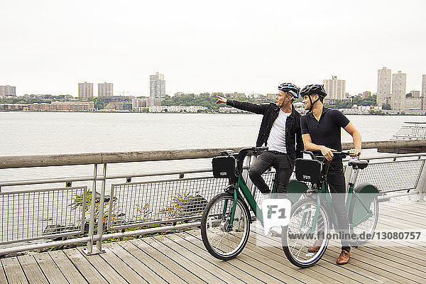 Man pointing and showing to friend while standing with bicycle on promenade
