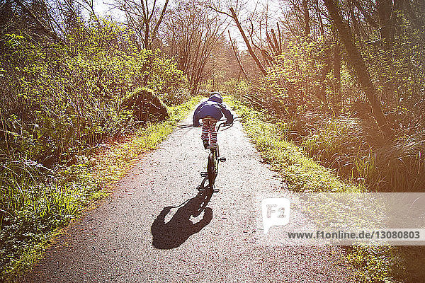 Rückansicht eines Mädchens  das bei sonnigem Wetter beim Fahrradfahren auf der Straße einen Stunt macht