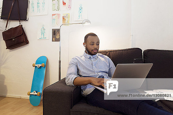 Illustratorin mit Laptop  während sie im Kreativbüro auf dem Sofa sitzt