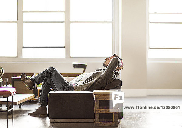 Side view of businessman relaxing on sofa in brightly lit creative office