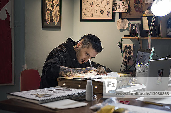 Male tattoo artist drawing on paper in studio