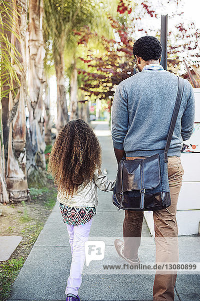 Rückansicht von Vater und Tochter beim Gehen auf dem Bürgersteig