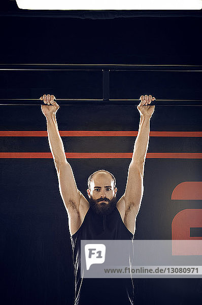 Porträt eines selbstbewussten männlichen Athleten  der im Fitnessstudio an einer Affenstange hängt