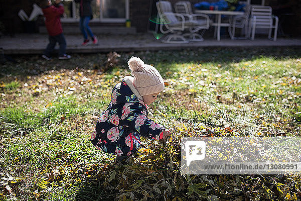 Kleines Mädchen  das im Herbst auf dem Feld im Hof an einem Laubhaufen spielt