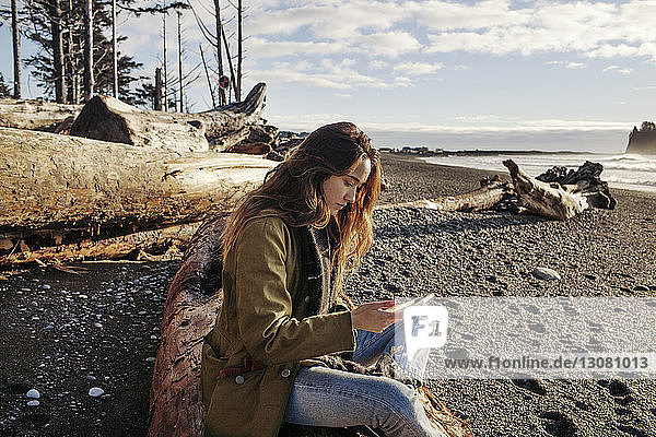 Seitenansicht einer Frau  die ein Smartphone benutzt  während sie am Strand sitzt