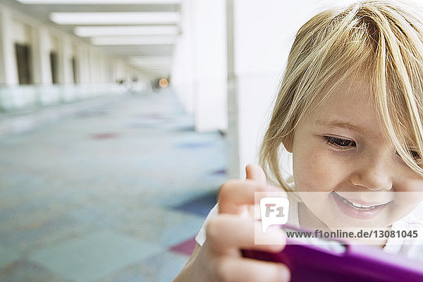 Lächelndes niedliches Mädchen spielt mit Smartphone auf dem Flur