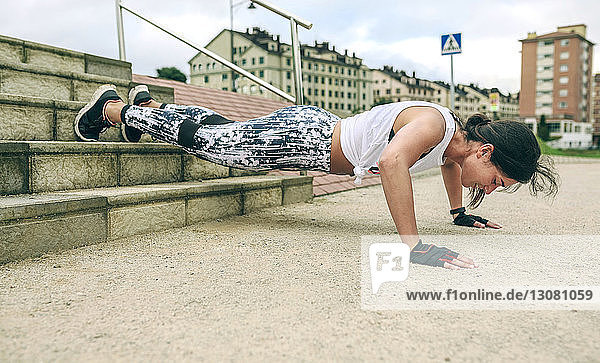 Frau in voller Länge beim Liegestützen auf Stufen im Park