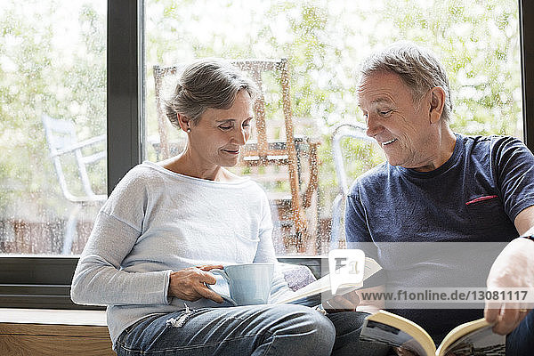 Glückliches älteres Ehepaar liest Bücher  während es zu Hause am Fenster sitzt