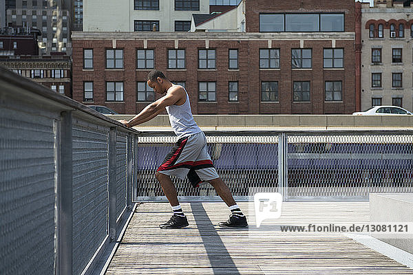 Seitenansicht eines Mannes  der sich auf einem Geländer an einer Strandpromenade gegen Gebäude lehnt