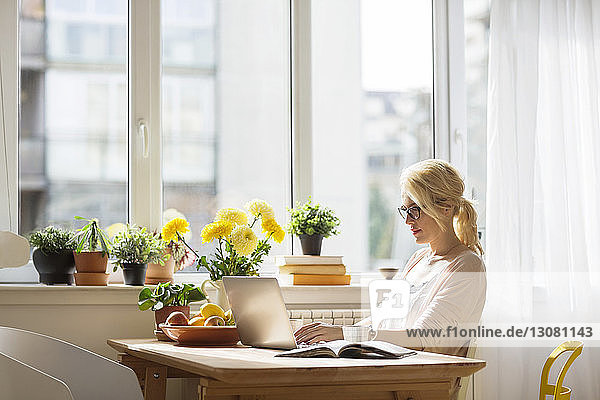 Frau benutzt Laptop-Computer  während sie zu Hause am Fenster sitzt