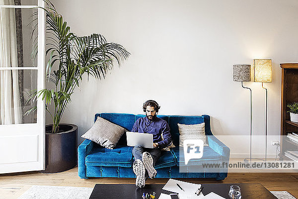 Kreativer Geschäftsmann hört Musik  während er im Büro mit seinem Laptop auf dem Sofa sitzt