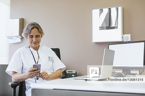 Senior female doctor using mobile phone while sitting at hospital