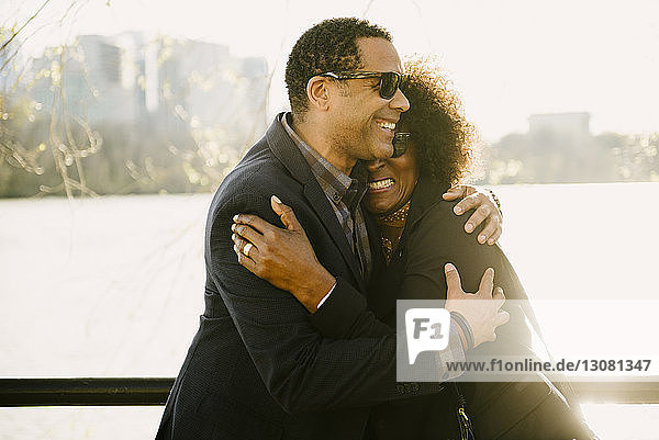 Glückliches Paar umarmt sich  während es in der Stadt am Geländer gegen den Fluss steht