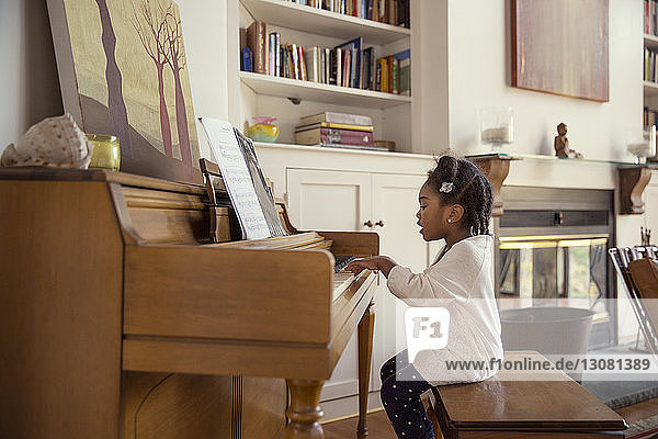 Side view of girl playing piano in living room
