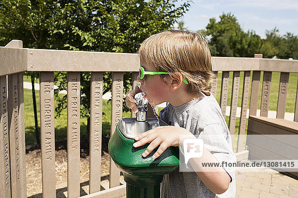 Boy drinking water from fountain at park