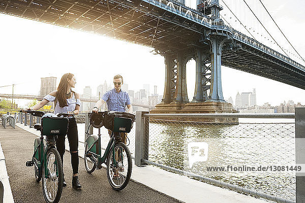 Paar zu Fuß mit Fahrrädern auf der Promenade am East River gegen die Manhattan-Brücke