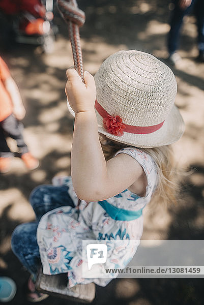 Playful girl wearing hat while swinging on rope swing