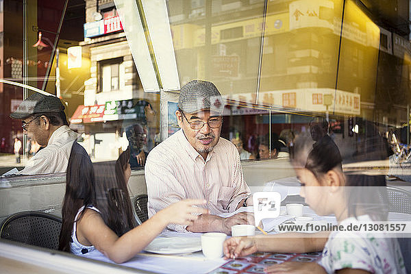 Grandfather with granddaughters sitting in restaurant seen through glass