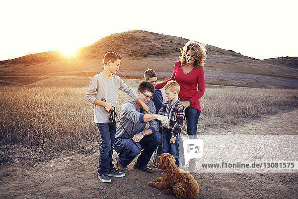 Family with dog enjoying on field against mountains on sunny day