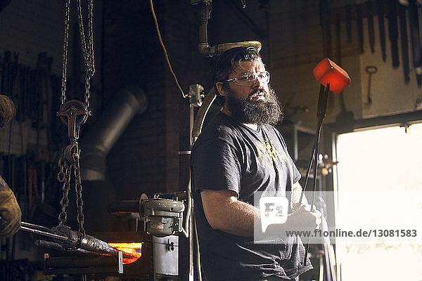 Schmied hält rotes  heißes Metall mit einer Zange in der Werkstatt