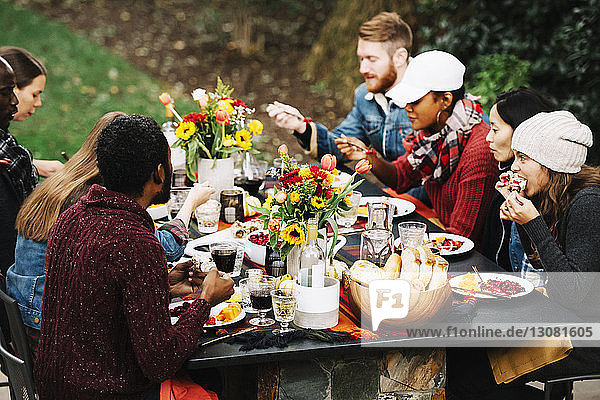 Schrägaufnahme von Freunden  die beim Essen am Esstisch im Garten sitzen