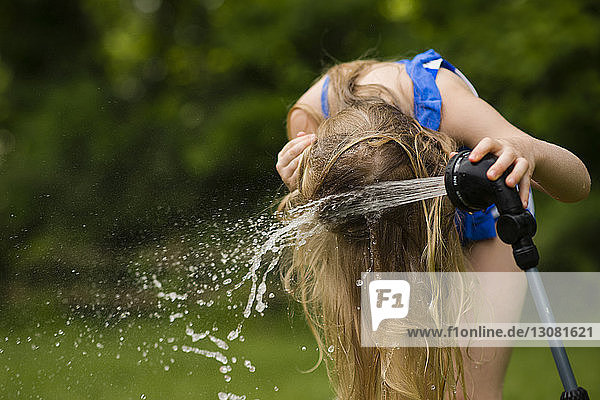 Girl pouring water on hair with hose at backyard