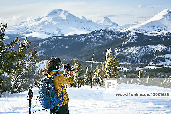 Rear view of female hiker photographing snowcapped mountains