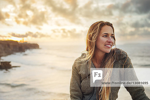 Lächelnde Frau schaut weg  während sie am Meer sitzt
