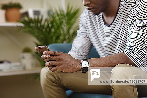 Mittelsektion eines Mannes  der ein Smartphone benutzt  während er zu Hause auf dem Sofa sitzt