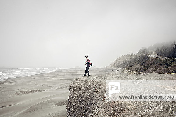 Side view of man standing on cliff at beach during foggy weather