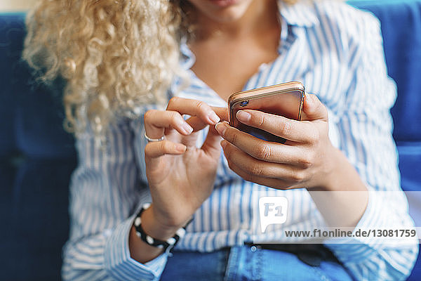 Midsection of woman using smart phone while sitting on sofa at home