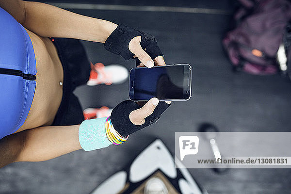 Draufsicht auf eine Sportlerin  die ein Smartphone im Fitnessstudio benutzt