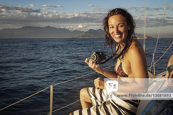 Porträt einer glücklichen Frau mit Kamera  die in einem Boot auf See reist