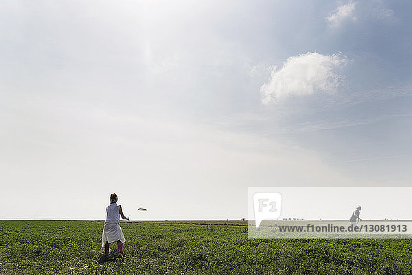 Couple playing with flying disc on grassy field against sky