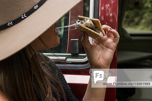 Close-up of woman eating smores while sitting by motor home at forest