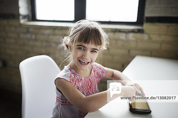 Porträt eines fröhlichen Mädchens  das zu Hause ein Smartphone benutzt