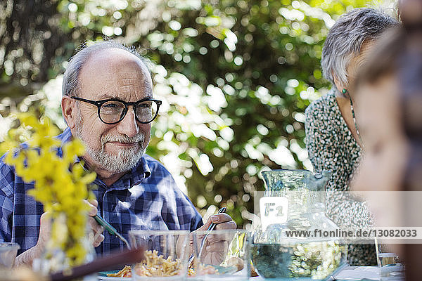 Lächelnder älterer Mann beim Essen mit Frau im Hof
