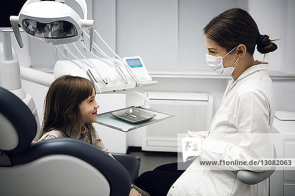 Glückliche Zahnärztin und Mädchen unterhalten sich in der Klinik
