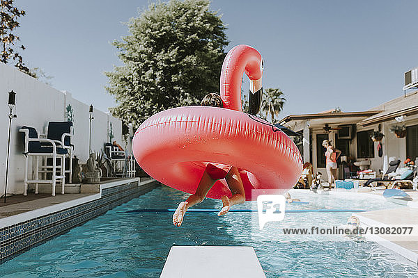 Mädchen springt mit rosa Flamingo ins Schwimmbad