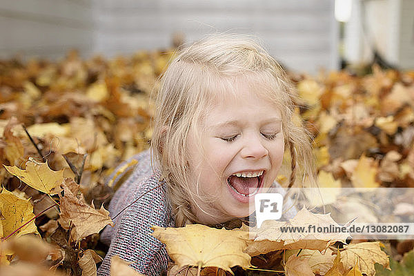 Fröhliches Mädchen spielt im Herbst mit Ahornblättern