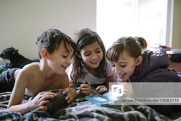 Glückliche Geschwister  die zu Hause im Bett ein Handy sehen