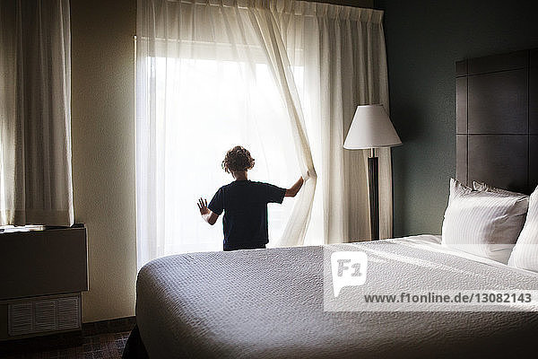 Rear view of girl looking though window in bedroom