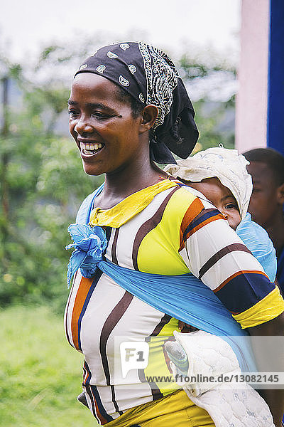 Fröhliche afrikanische Frau  die ein Mädchen in Stoff trägt