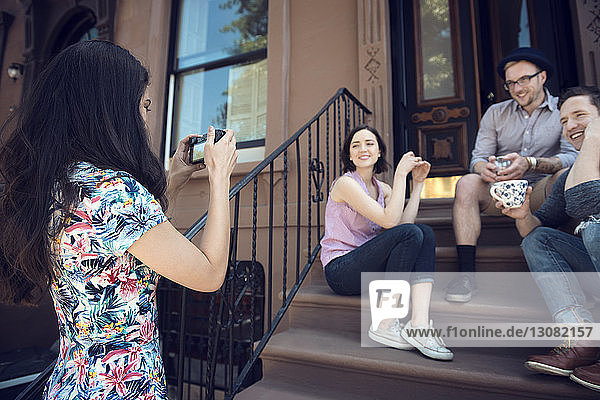 Frau fotografiert Freunde  die auf Stufen vor dem Gebäude sitzen